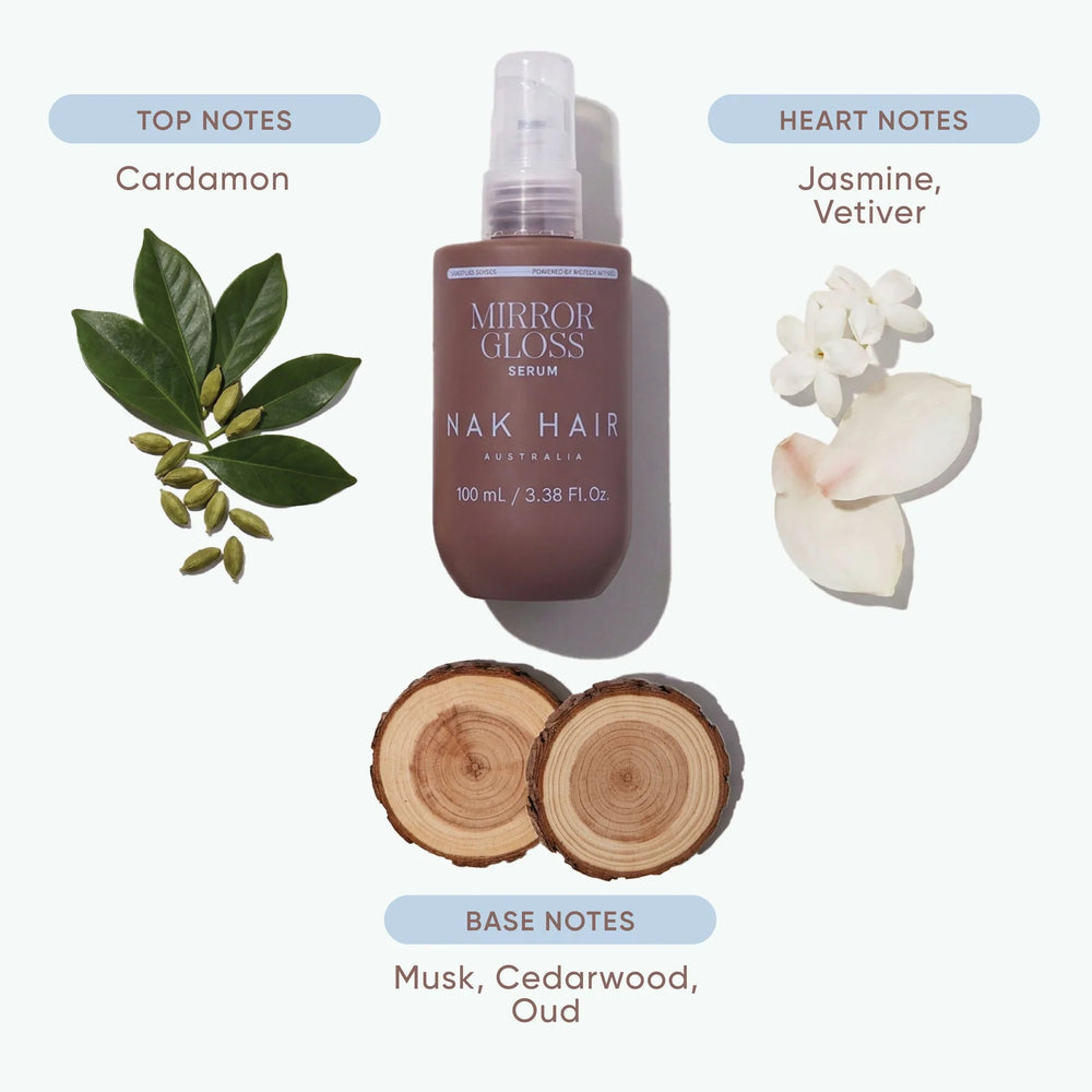 Mirror Gloss Silk Nak Hair Fragrance Spray bottle centered on a light gray background, surrounded by botanical and wood notes: cardamon leaves, jasmine and vetiver flowers, and cedarwood slices. Text reads 'THE FRAGRANCE MORE THAN ROUTINE' with top and base notes labeled.