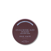 A round dark mauve-brown tin of NAK HAIR Hyaluronic Acid Polish Hair & Body Scrub on a clean white background.