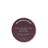 A round dark mauve-brown tin of NAK HAIR Hyaluronic Acid Polish Hair & Body Scrub on a clean white background.
