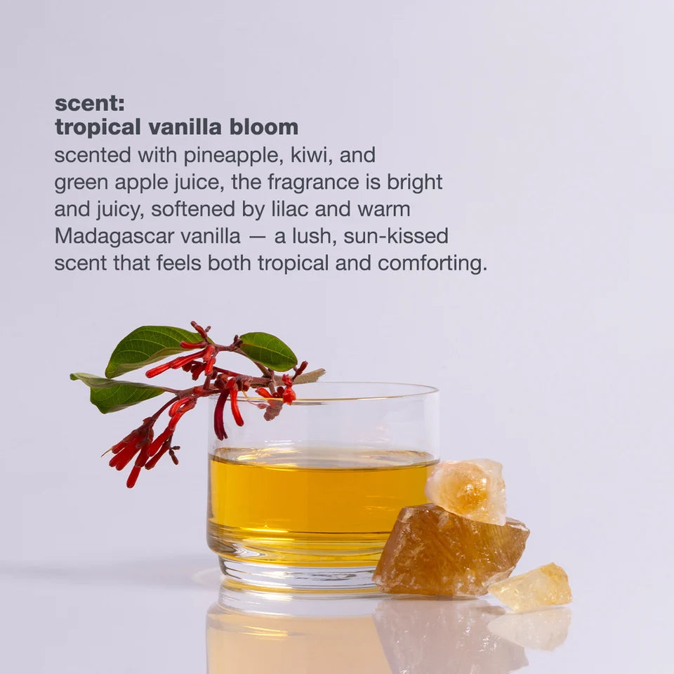 Glass of yellow liquid with a tropical vanilla bloom branch and ginger root on a light gray background