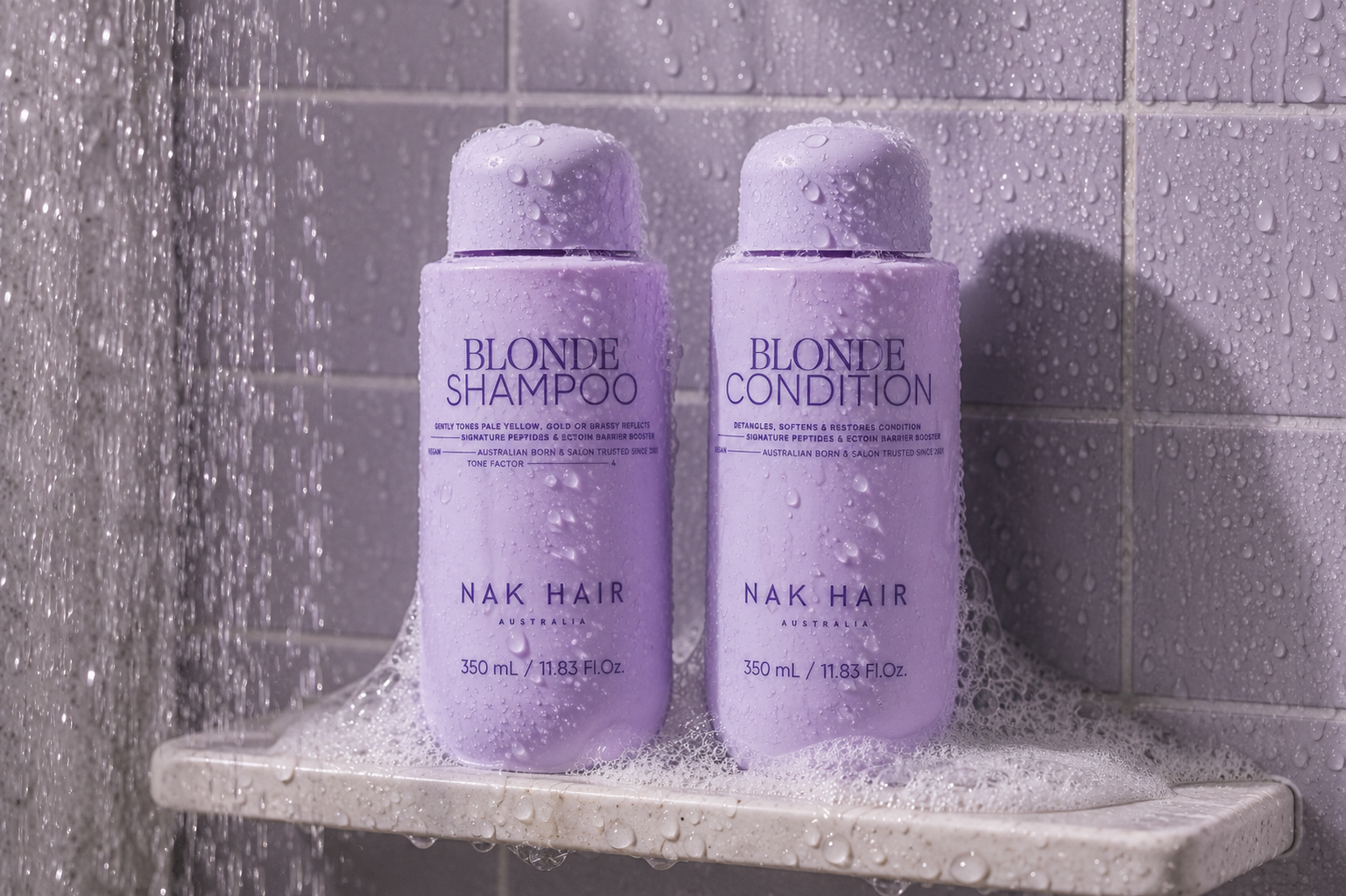 Two bottles of Blonde Shampoo and Conditioner by Nak Hair on a shower ledge.