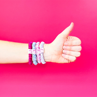 Hand giving a thumbs up with colorful hair ties on a pink background