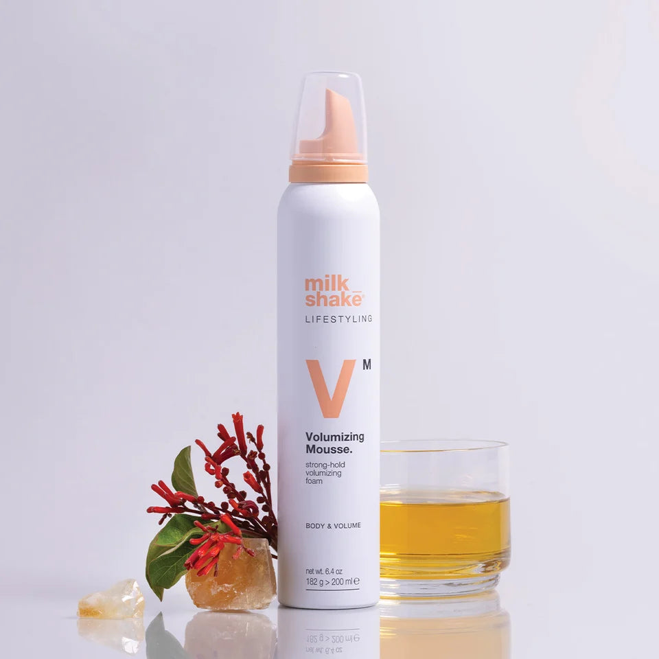 Milk Shake Volumizing Mousse bottle with a glass of liquid on a light gray background